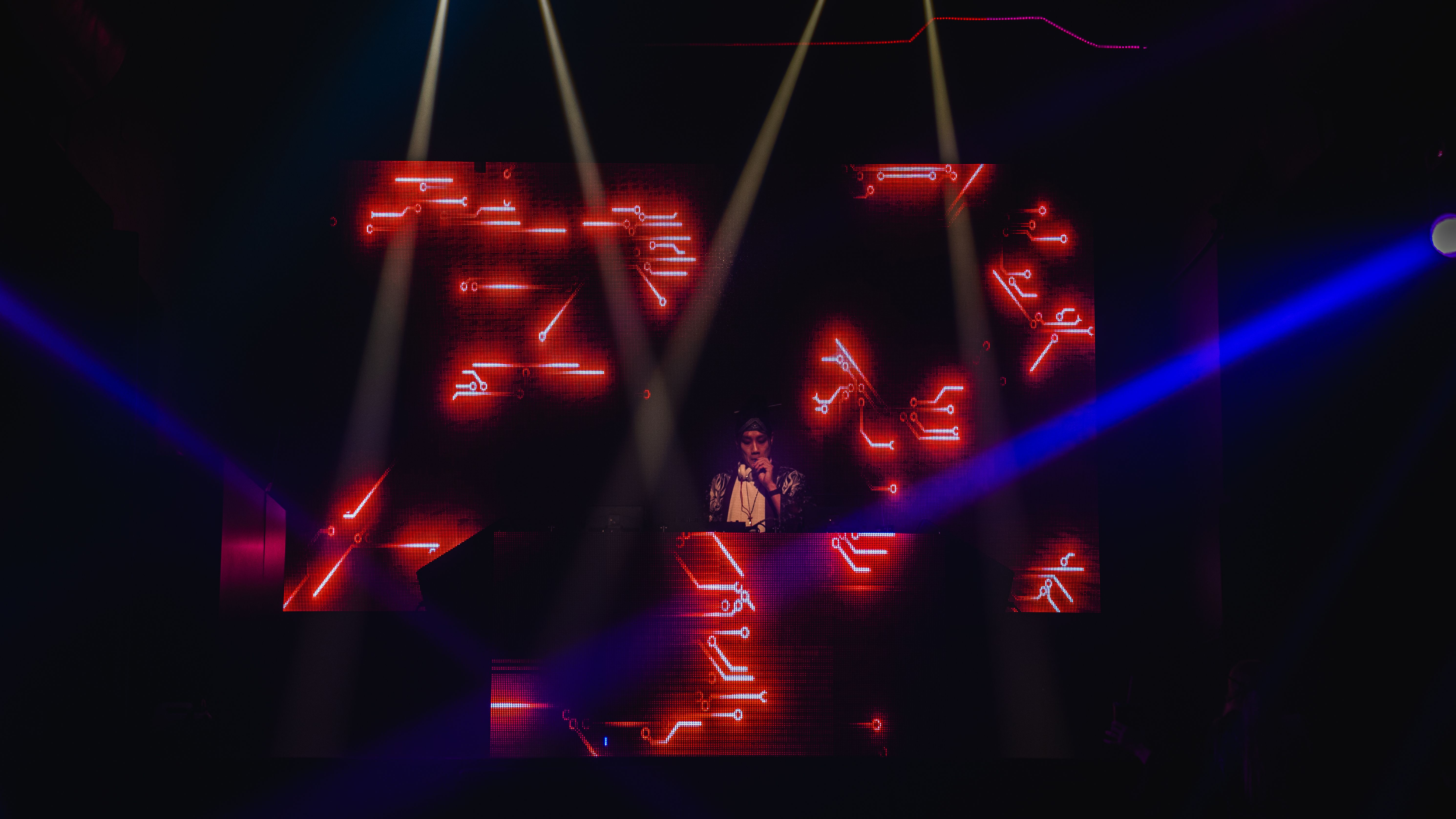 DJ no palco diante de painéis vermelhos iluminados.