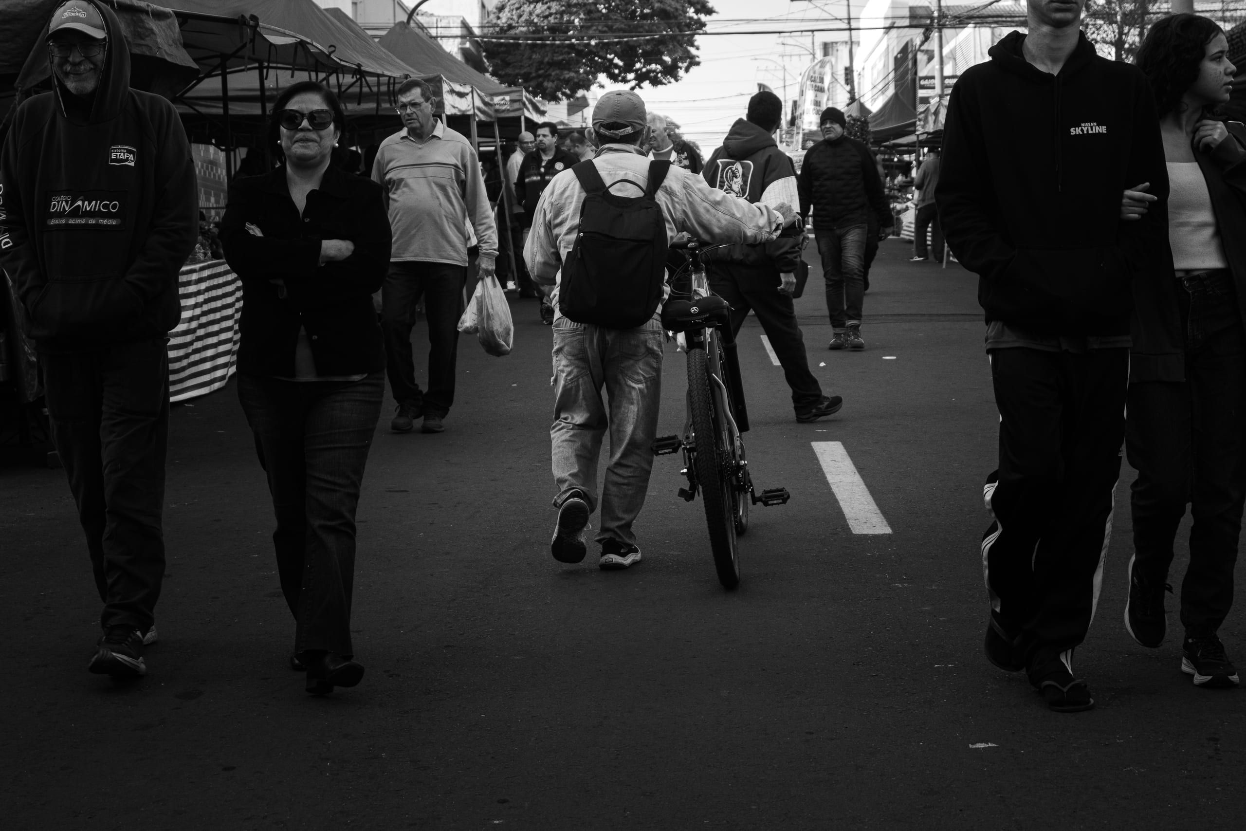 Pessoas circulam por um corredor de feira; uma delas leva uma bicicleta.