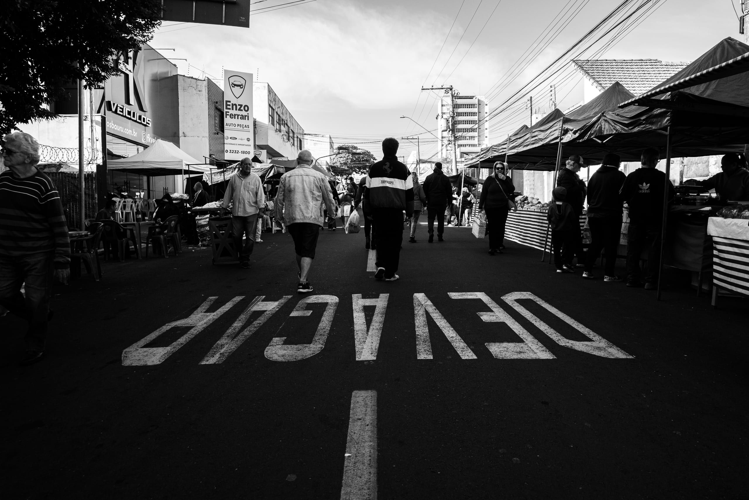 Pessoas caminham entre barracas em um corredor da feira.