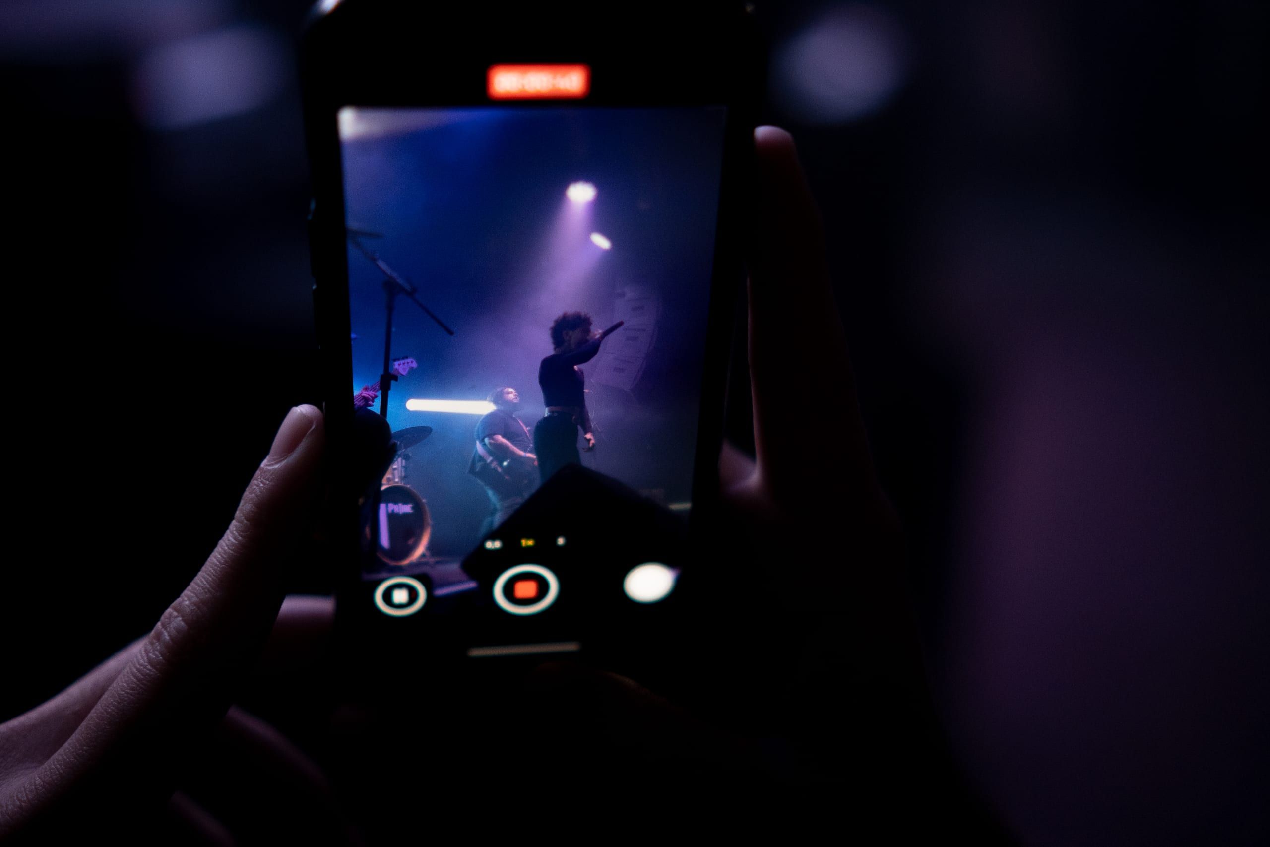 Uma mão segura um telefone que enquadra o palco sob luz violeta.