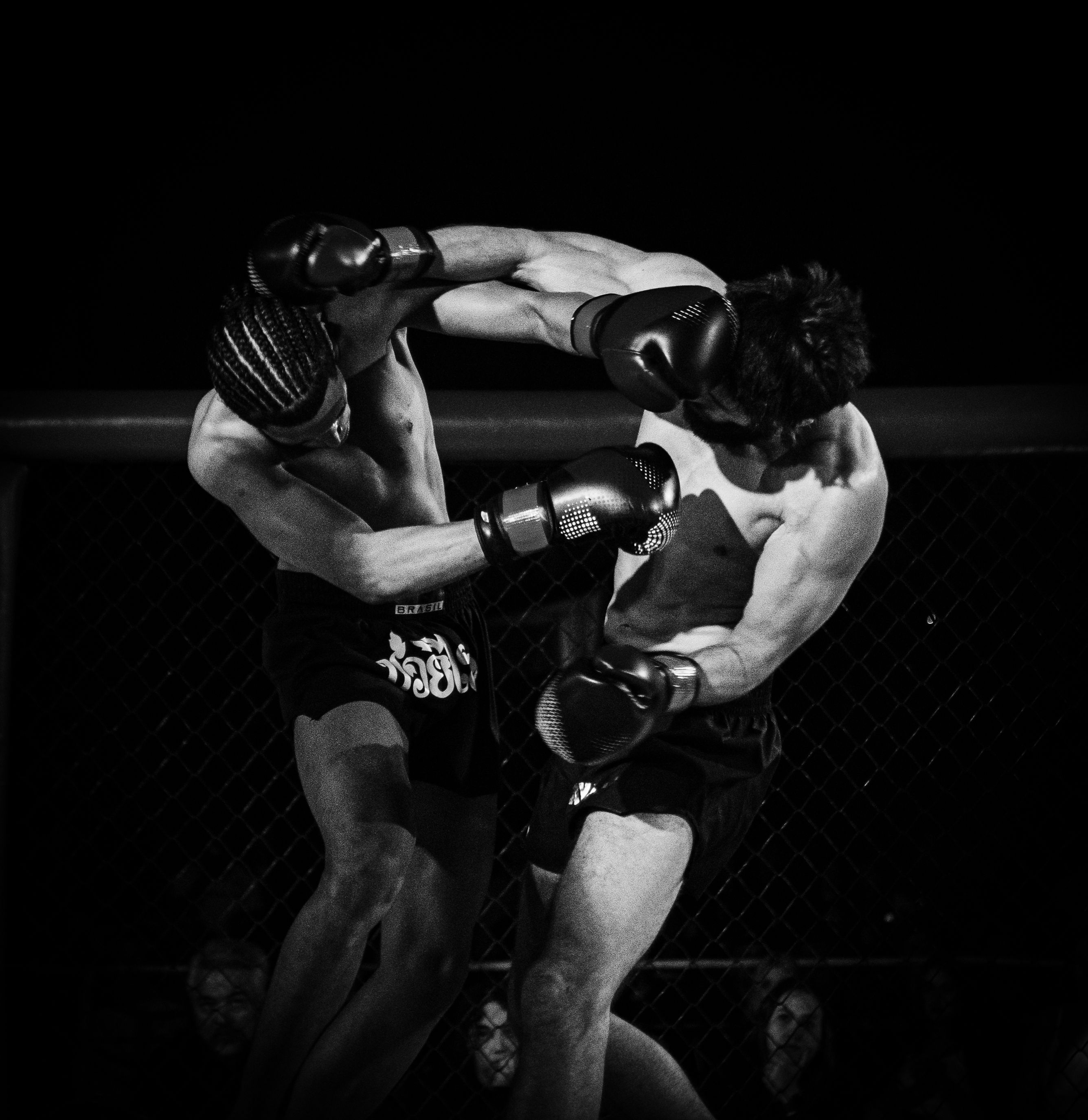 Os lutadores trocam golpes junto à grade do ringue.