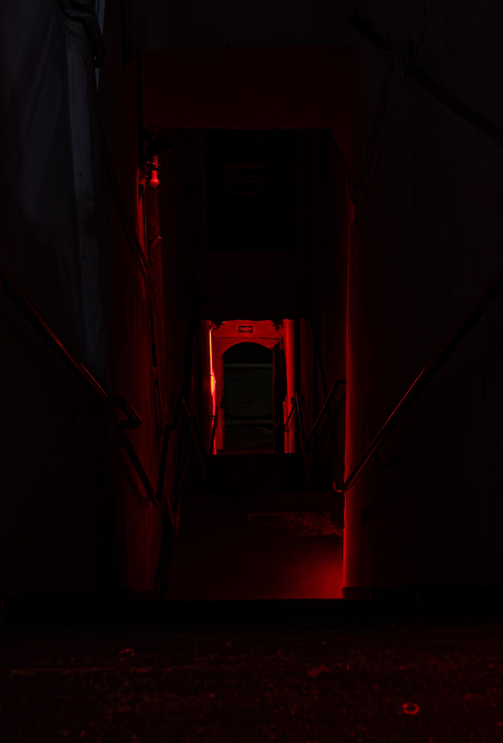 Corredor interno escuro com uma abertura iluminada em vermelho ao fundo.