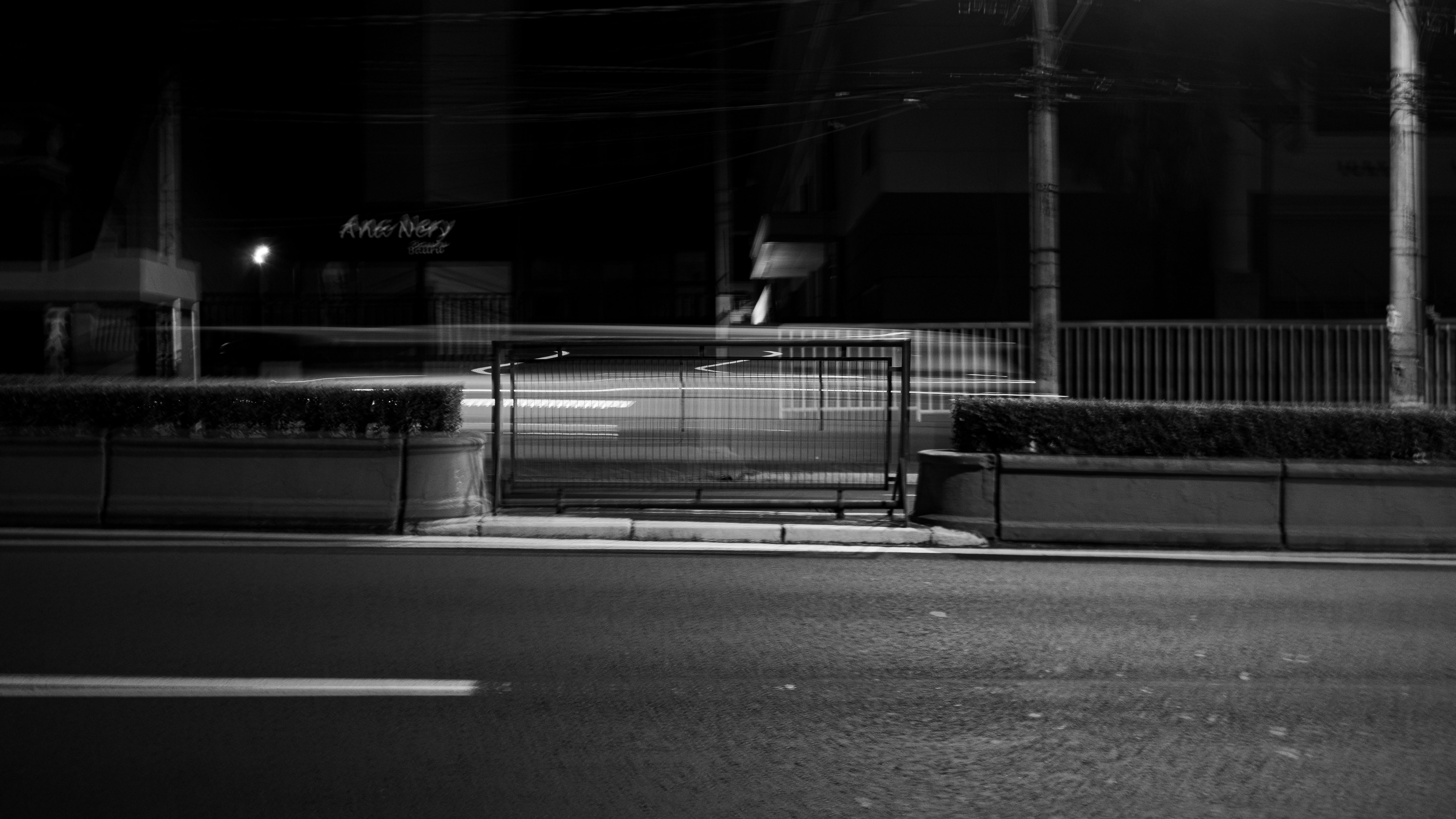 Calçada e estruturas do lado oposto da rua em uma fotografia noturna em preto e branco.